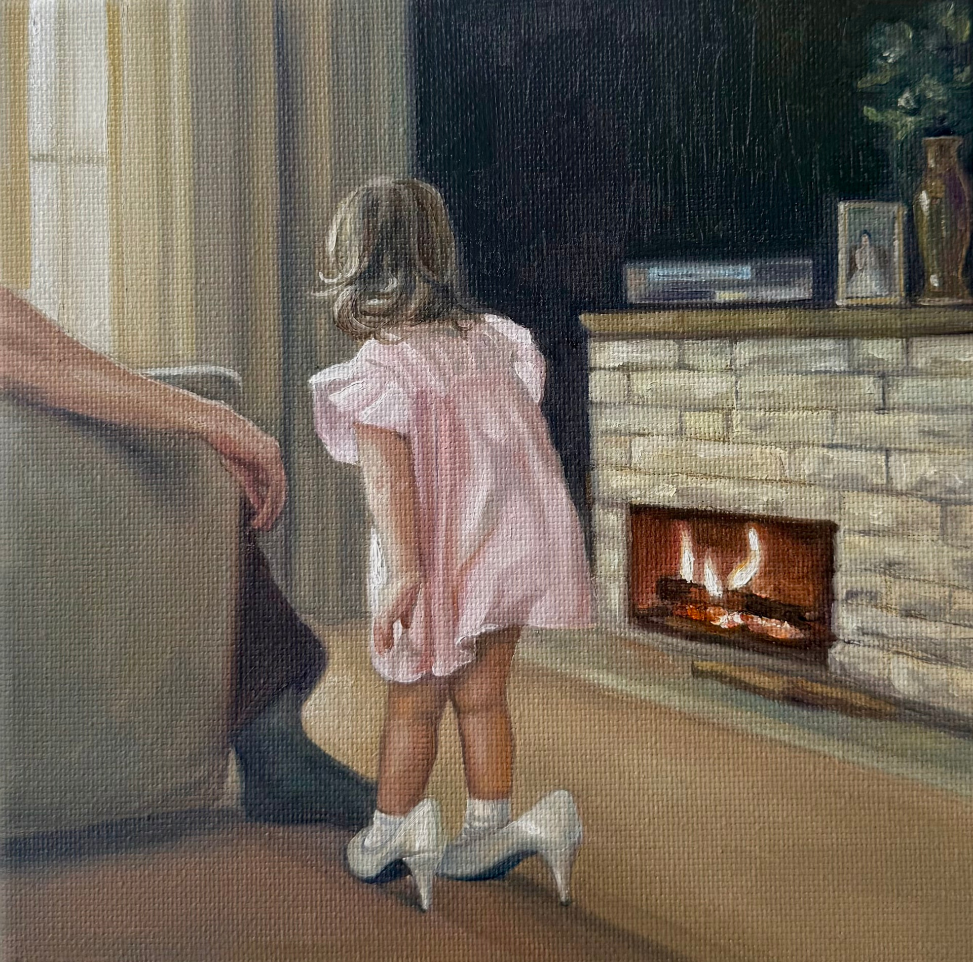 A small girl in a pink dress wearing grown-up heels by a fireplace